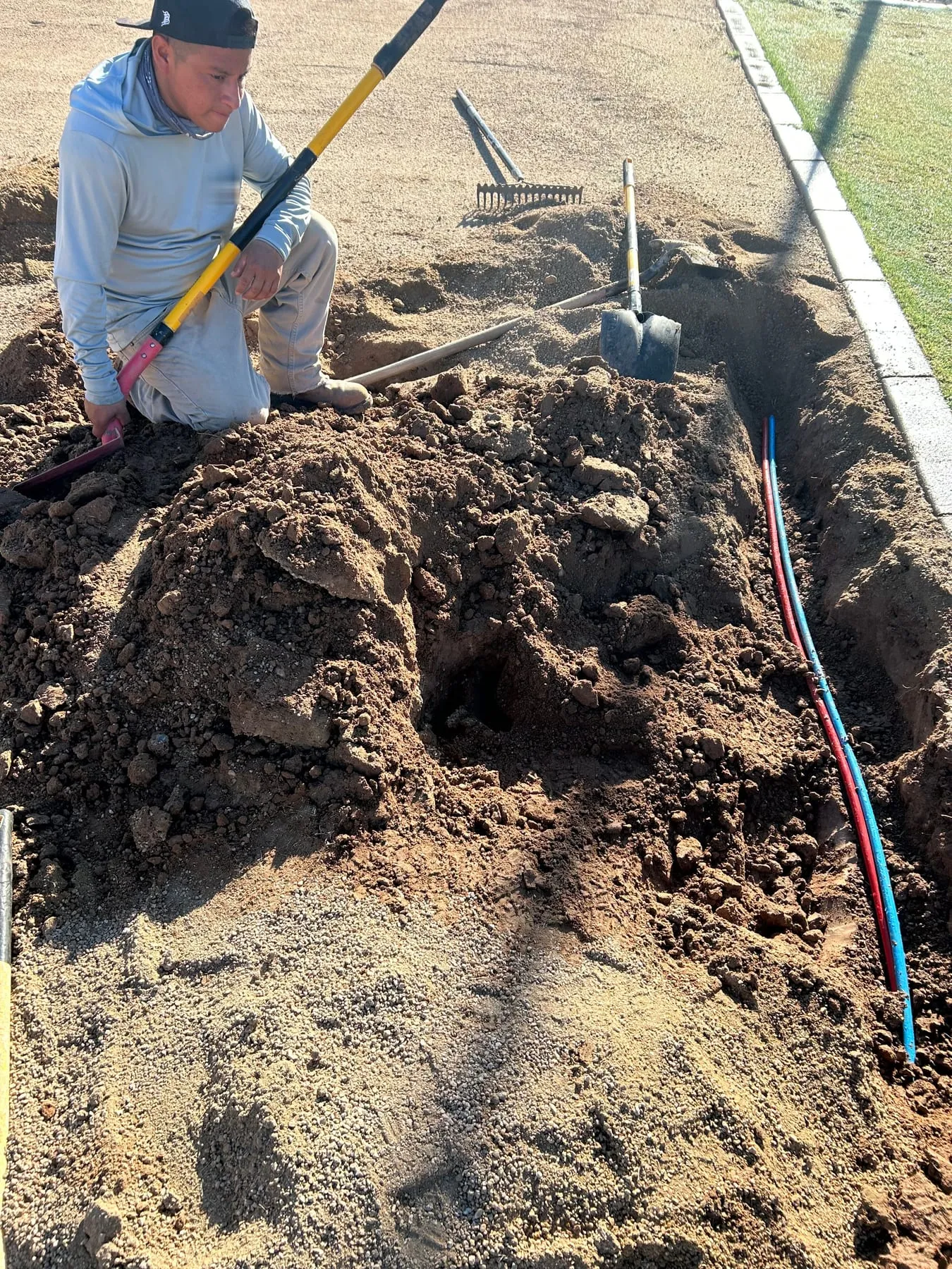 Crew member kneeling beside a trench with new irrigation tubing laid along a curb