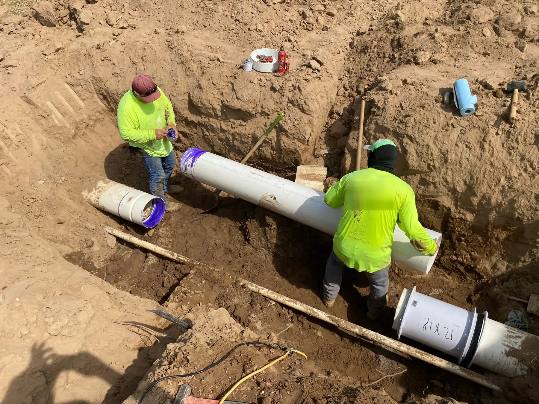 Two crew members joining large-diameter PVC pipe in a deep trench