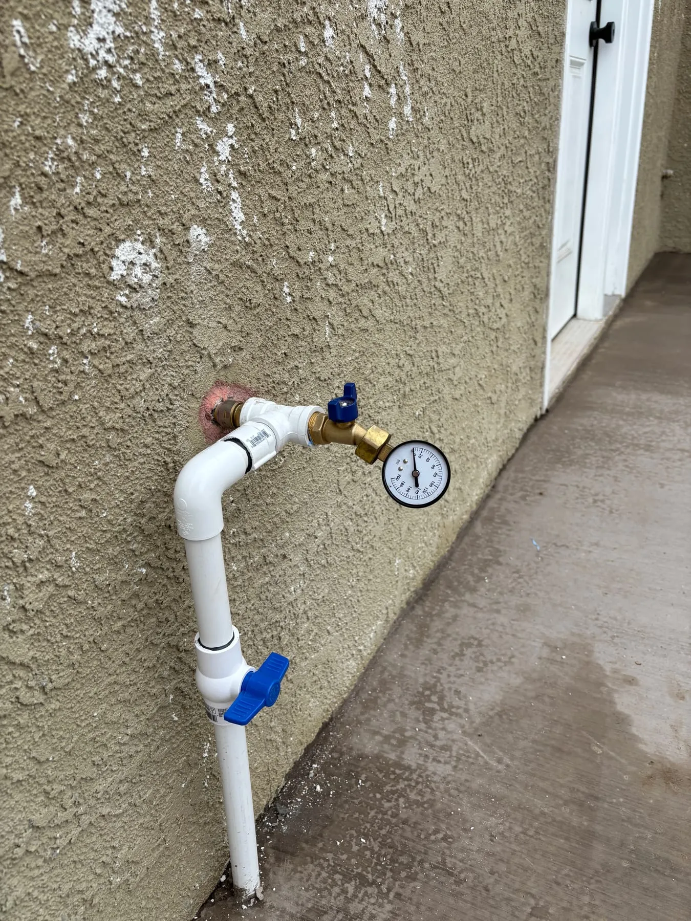 Pressure gauge fitted to a PVC irrigation supply riser on a stucco wall