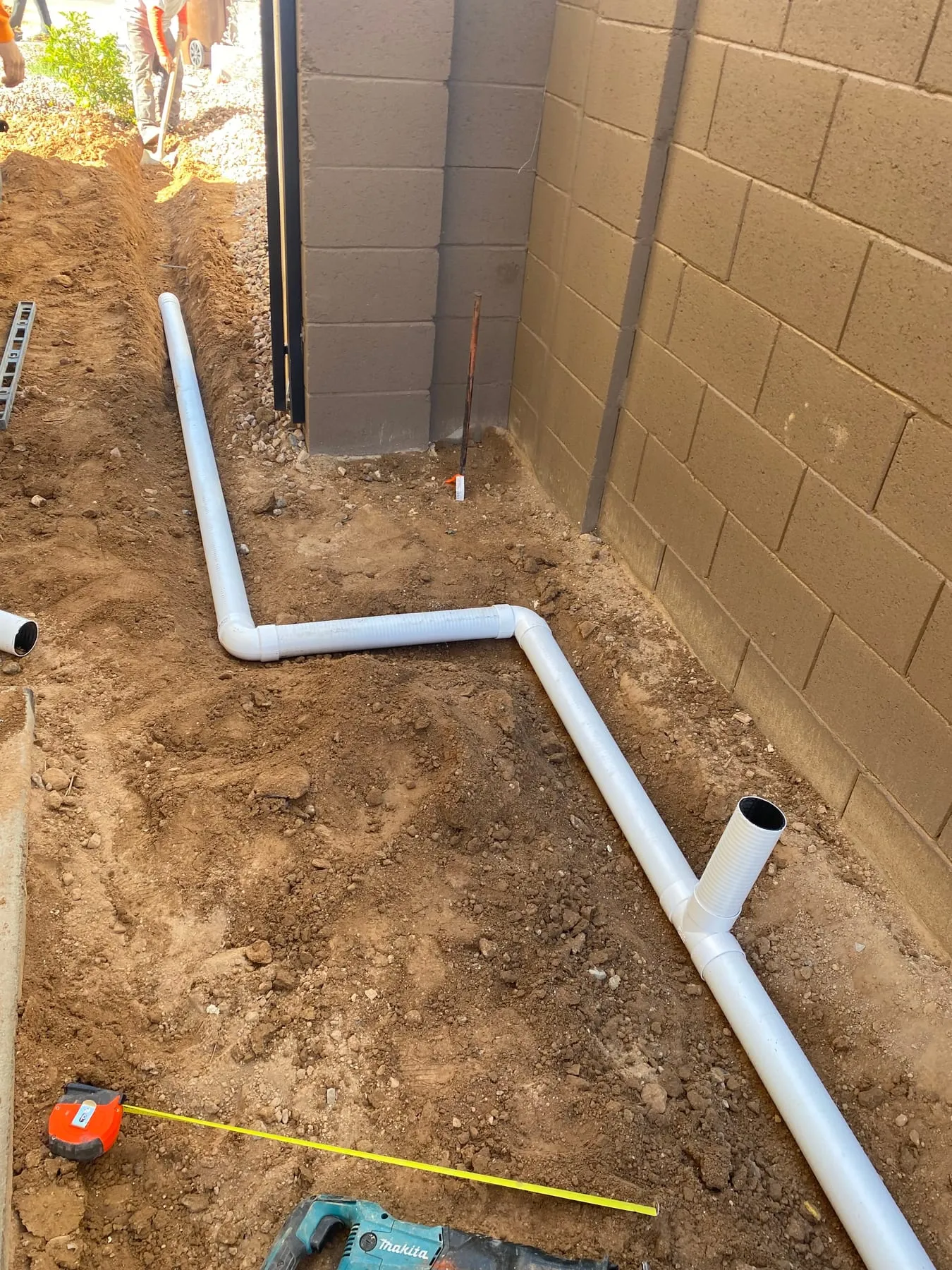 New PVC irrigation pipe laid along a block wall before backfill