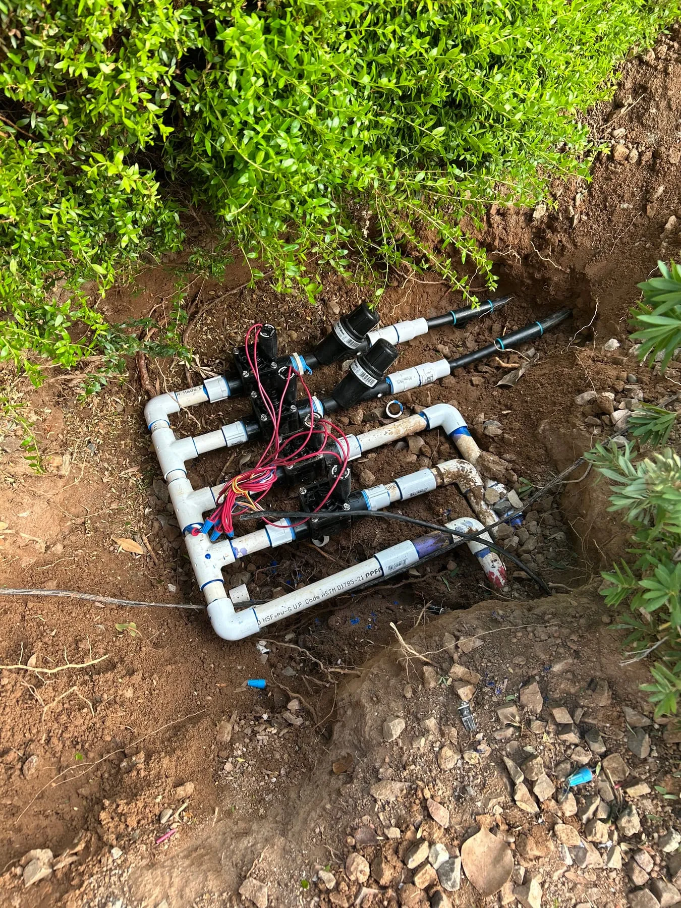 New irrigation valve manifold with wired solenoid valves, plumbed in PVC beside a planting bed